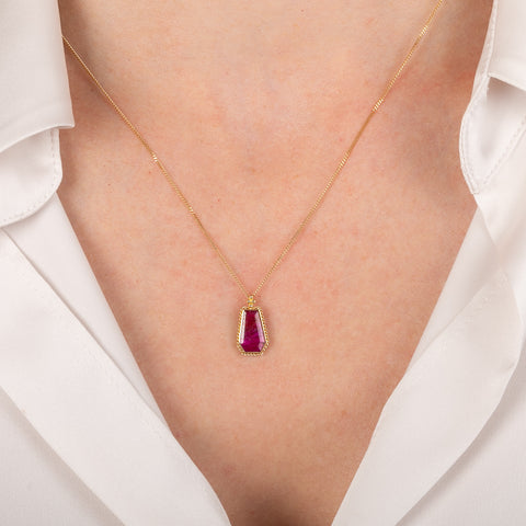 Gold necklace with a red ruby gemstone pendant on a person wearing a white shirt.