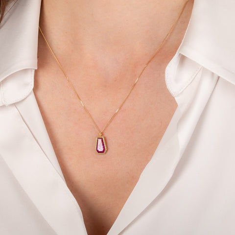 Necklace with a ruby gemstone pendant worn by a person in a white shirt.