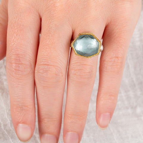 Hand wearing an aquamarine ring with 18k gold bezel and sterling silver band on white background