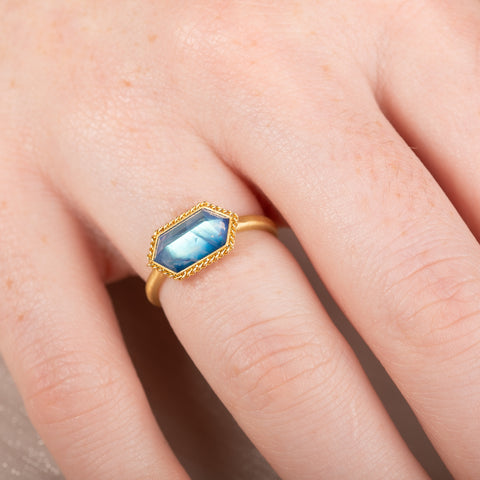 Gold ring with a moonstone gemstone on a person's finger