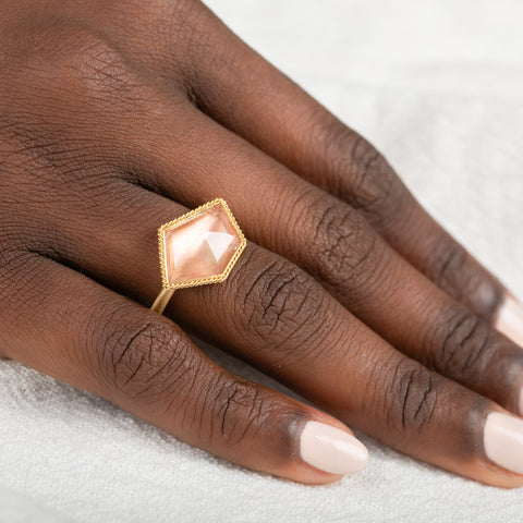 Hand wearing a gold ring with an Oregon sunstone gemstone on a light background