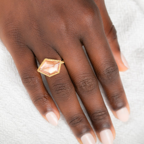 Hand wearing a gold ring with an Oregon sunstone gemstone on a light background