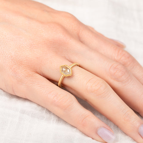 Gold ring with a golden colored diamond on a person's finger against a light background
