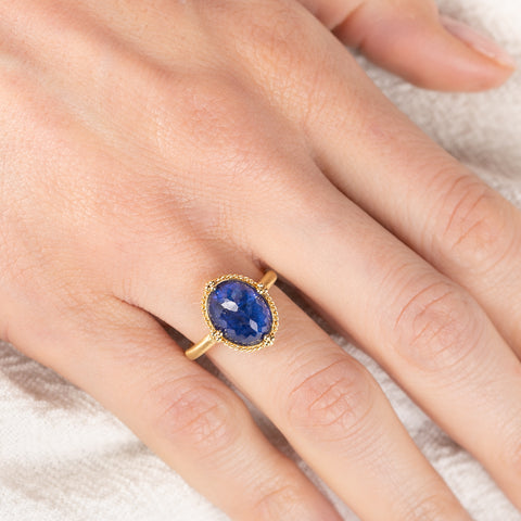 Gold ring with a blue tanzanite gemstone on a hand against a neutral background