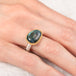 Ring with a labradorite gemstone on a finger against a white background