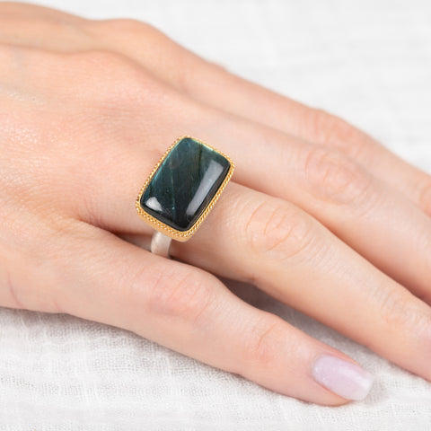 Gold ring with a labradorite stone on a hand against a white background