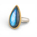 Ring with a teardrop-shaped labradorite gemstone and gold bezel with silver band on a white background