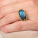 Gold ring with a labradorite gemstone on a person's finger