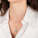 Gold necklace with a labradorite pendant worn by a person in a white shirt