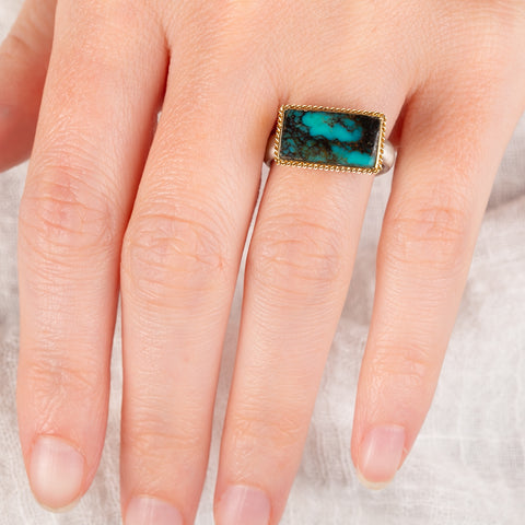Hand wearing a turquoise ring with gold bezel and sterling silver band