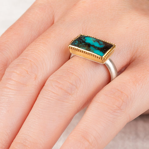 Close up of hand wearing a turquoise ring with gold bezel and sterling silver band