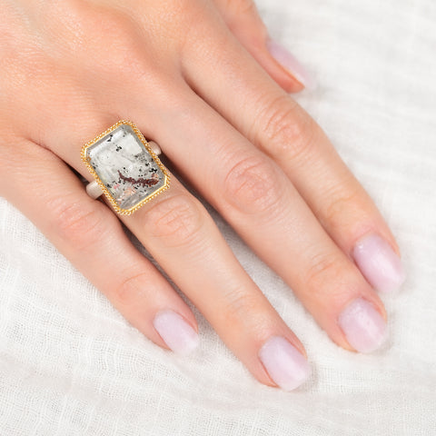 Ring with a lodolite quartz stone on a finger against a white background