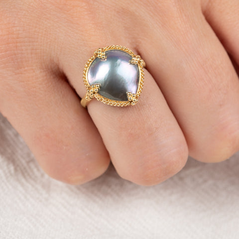 Gold ring with a mabe pearl on a person's finger