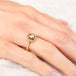 Gold ring with a diamond gemstone on a hand against a neutral background
