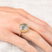 Gold ring with a topaz stone on a person's finger against a neutral background
