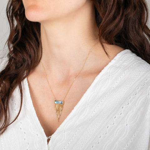 Woman wearing a gold necklace with a moonstone pendant on a plain background