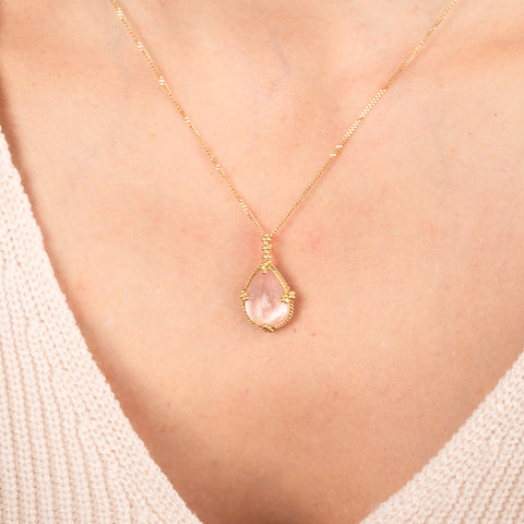 Gold necklace with a morganite teardrop pendant on a person's neck