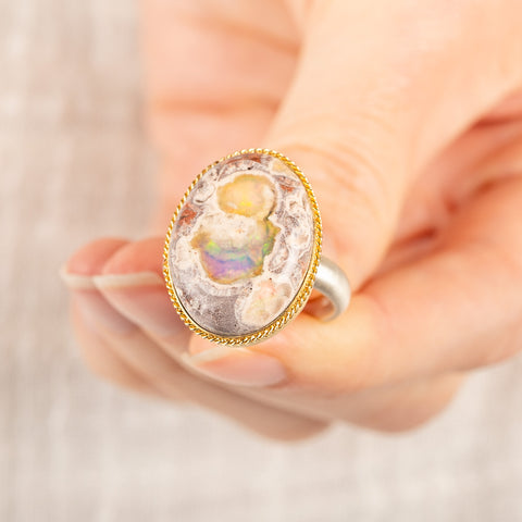 A close up of someone holding a handmade ring with a Mexican Opal stone set in an 18k gold bezel with a sterling silver band