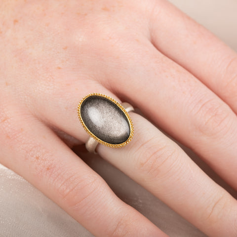Obsidian ring with gold setting and silver band on a person's finger