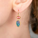 Close-up of a person wearing gold earrings with colorful gemstones.