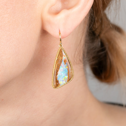 Gold-framed teardrop earrings with opalized wood stones worn by a person