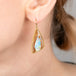 Gold-framed teardrop earrings with opalized wood stones worn by a person