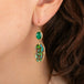 Pair of gold earrings with emerald and opalized wood stones worn by a person