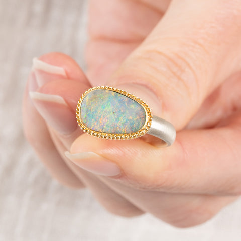 Close up of person holding a handmade fine jewelry boulder opal ring with an 18k gold bezel and sterling silver band