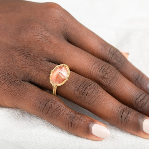 Gold ring with an Oregon sunstone on a person's finger against a neutral background