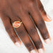 Gold ring with an Oregon sunstone on a person's finger against a neutral background