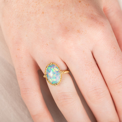 Gold ring with an Ethiopian opal stone on a person's hand