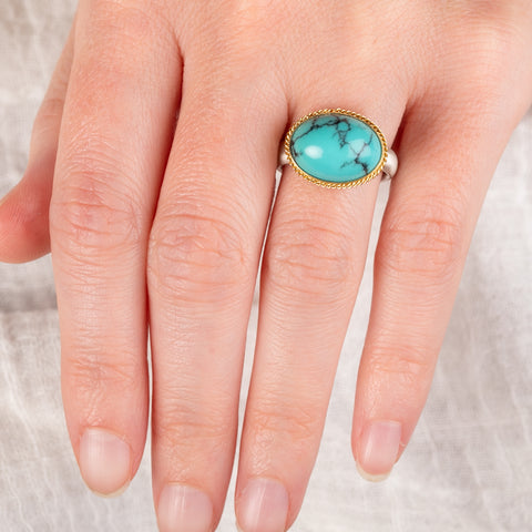 Hand wearing a turquoise ring with gold bezel and sterling silver band on white background