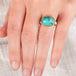 Hand wearing a turquoise ring with gold bezel and sterling silver band on white background