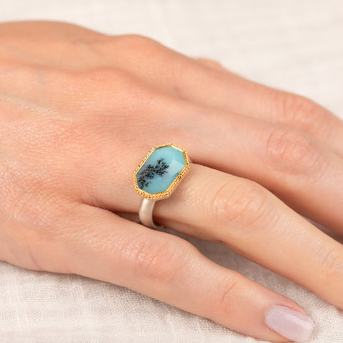 Gold and silver ring with peruvian opal stone on a hand against a neutral background