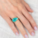 Hand wearing a peruvian opal ring with gold bezel and silver band on a white fabric background
