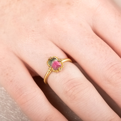 Gold ring with a watermelon tourmaline gemstone worn on a persons finger