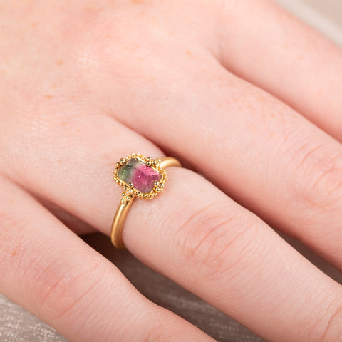 Gold ring with a watermelon tourmaline gemstone worn on a persons finger