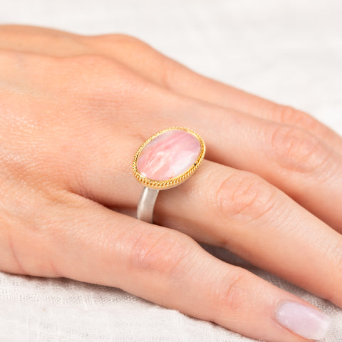 Gold and silver ring on a person's finger with a pink opal stone
