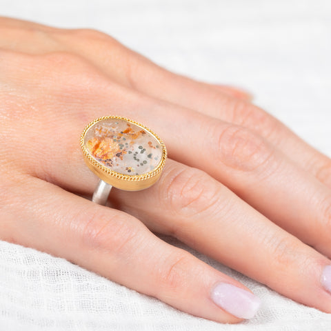 Gold and silver ring with a quartz with pyrite stone on a hand against a white background