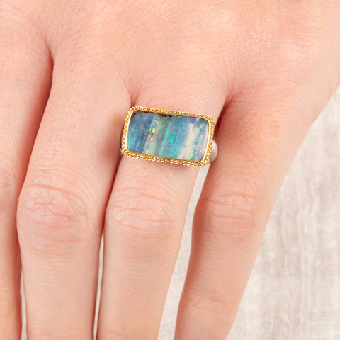 Close up of person wearing a handmade fine jewelry boulder opal ring with an 18k gold bezel and sterling silver band