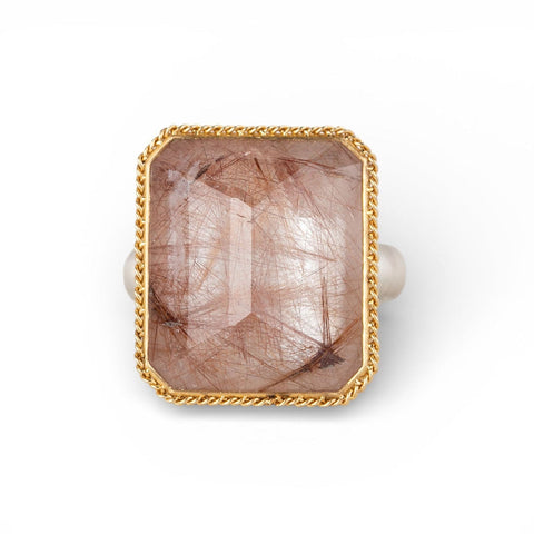 Ring with a rutilated quartz stone, gold bezel and silver band on a white background