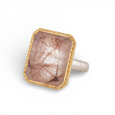 Ring with a gold bezel, silver band and rutilated quartz stone on a white background