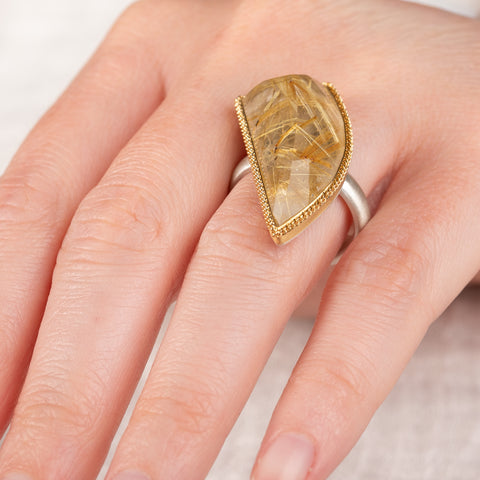A hand wearing a rutilated quartz ring with an 18k gold bezel and sterling silver band