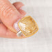 Gold and silver ring with a rutilated quartz gemstone held by a hand on a light background