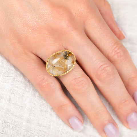 Ring with a gold bezel, silver band and rutilated quartz stone on a hand against a white background