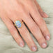 Hand wearing a ring with an opal stone on a light fabric background