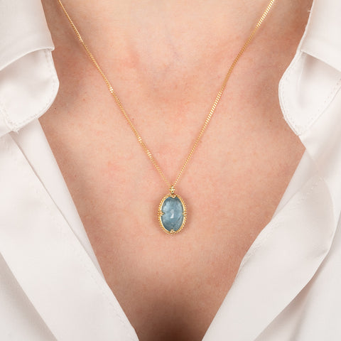 Gold necklace with an aquamarine worn by a person in a white shirt.