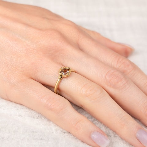 Gold ring with a brown diamond on a hand against a neutral background