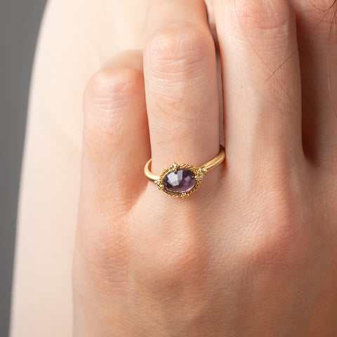 Gold ring with a spinel gemstone on a person's finger against a neutral background