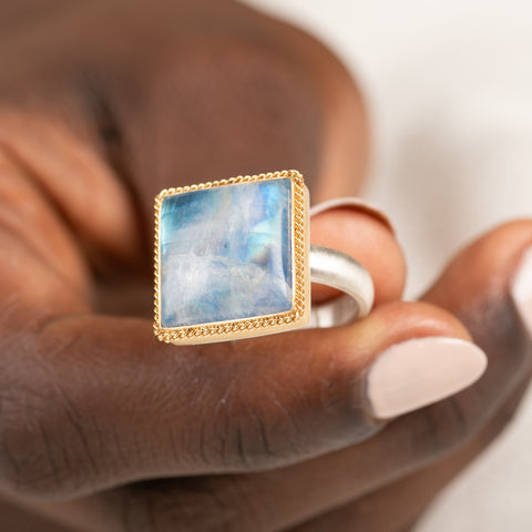 Gold and silver ring with a moonstone held in hand against a white background